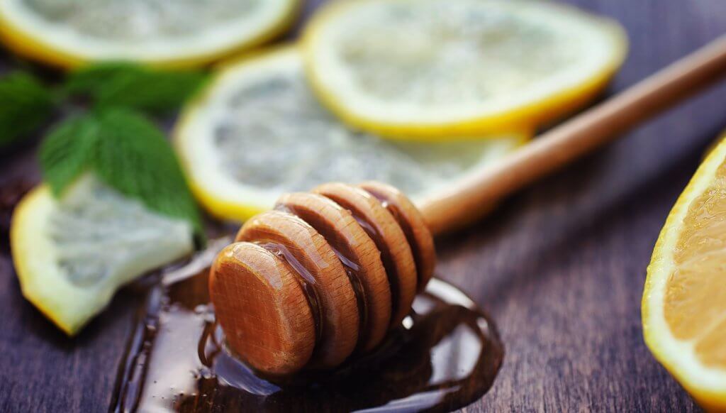 Honey and lemon. Honey stick and slices of sliced lemon on wooden table. Tea in a cup and sweet lime honey in a jar.