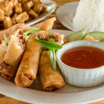 Filipino Lumpia Shanghai or Lumpiang Shanghai, a Filipino egg roll, with Sizzling tofu and a cup of rice at the back. Philippine cuisine.
