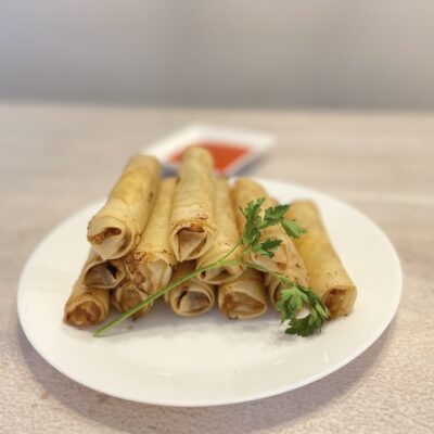 Filipino Lumpia Shanghai on a white plate with Sweet Chili sauce at the back